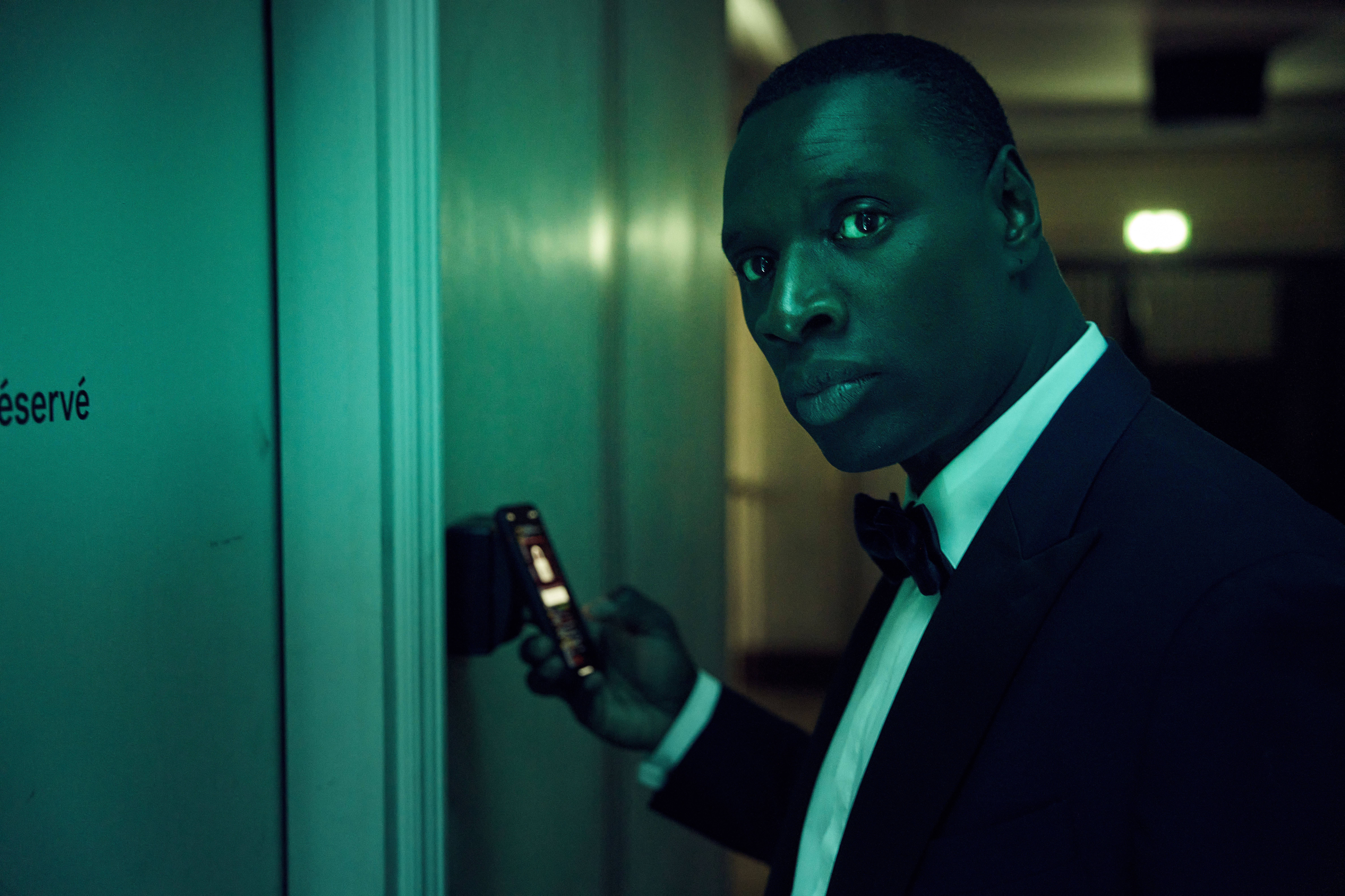 Omar Sy as Lupin in a formal tuxedo holding a cellphone in Lupin.