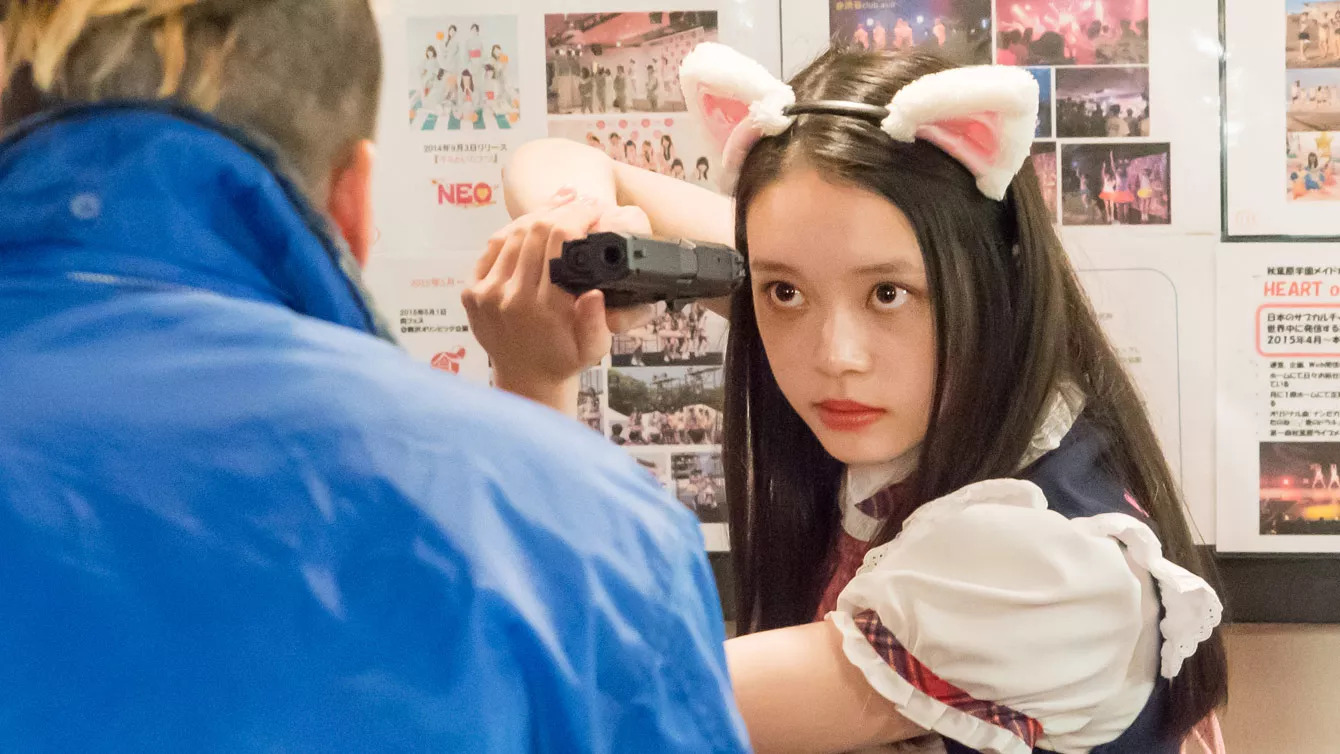 A long-haired girl (Akari Takaishi) in a maid outfit with bunny ears aims a pistol sideways at a man in a blue rain jacket in Baby Assassins.