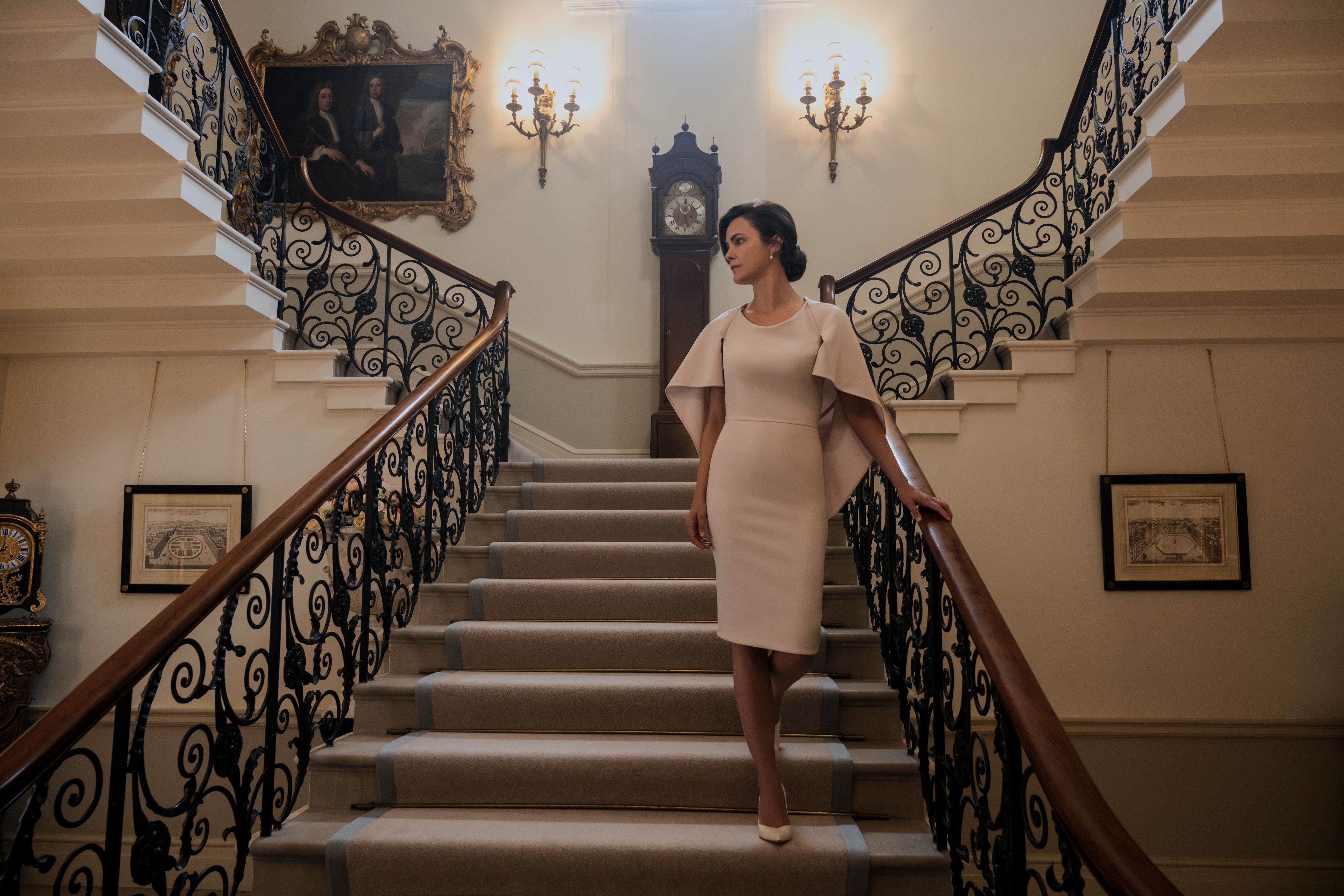 Keri Russell walks down an extravagant staircase while wearing a fancy beige-ish dress in The Diplomat.
