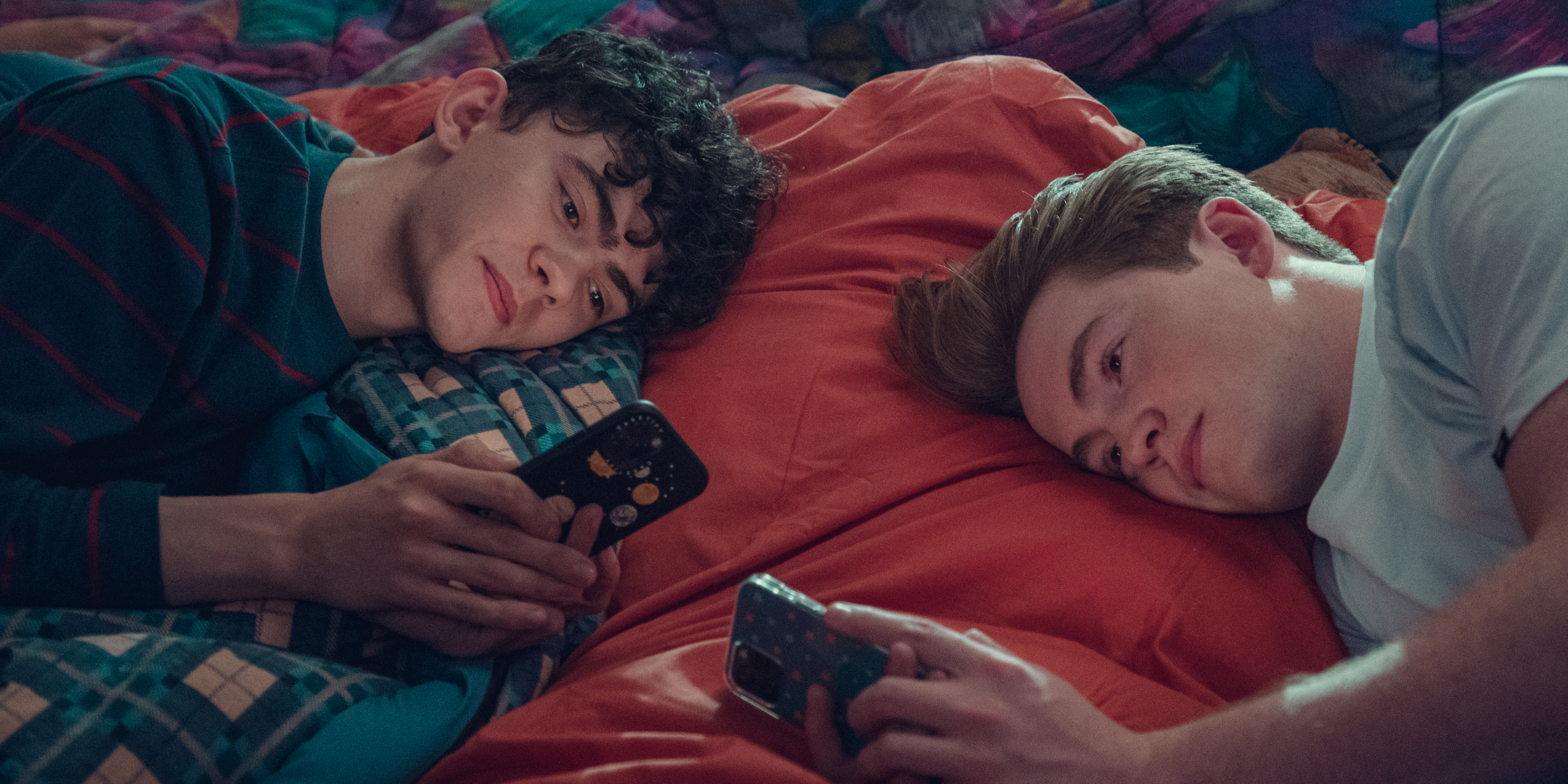 Nick and Charlie, from Heartstopper, laying side by side, looking at their phones.