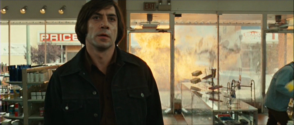 Anton Chigurh (Javier Bardem) walking through a grocery store as a explosion erupts in the street outside in No Country for Old Men.